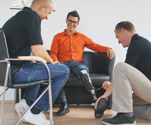 Anprobe, Orthopädietechniker macht Anpassungen an der Beinprothese des Kunden, dritte Person sitzt links
