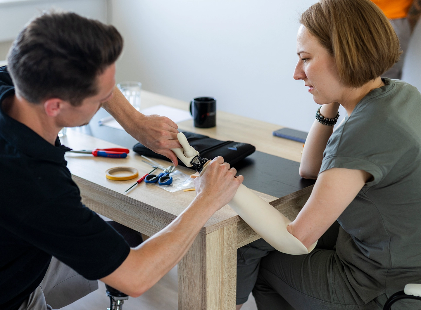 Techniker korrigiert Hand einer Armprothese der Kundin die vor ihm sitzt