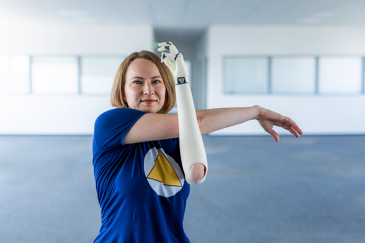 Frau macht Dehnübung mit einer Armprothese und schaut in die Kamera