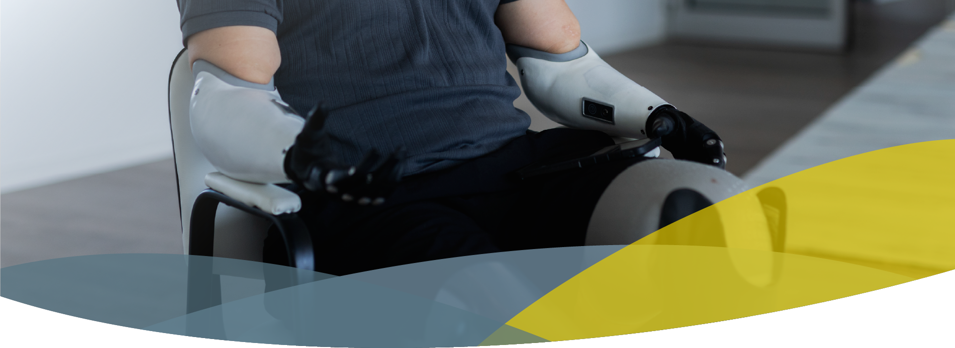 Headerbild für über uns seite bei APT Prothesen, Person trägt zwei Armprothesen und zwei Armprothesen, sitzt auf einem Stuhl in der APT-Filiale