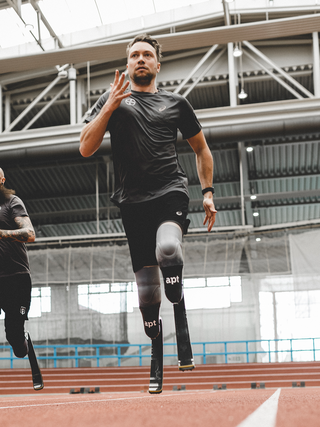 David Behre beim Sprint über eine Tartanbahn in dunklen Sportklamotten und zwei Sportprothesen mit APT Schriftzug
