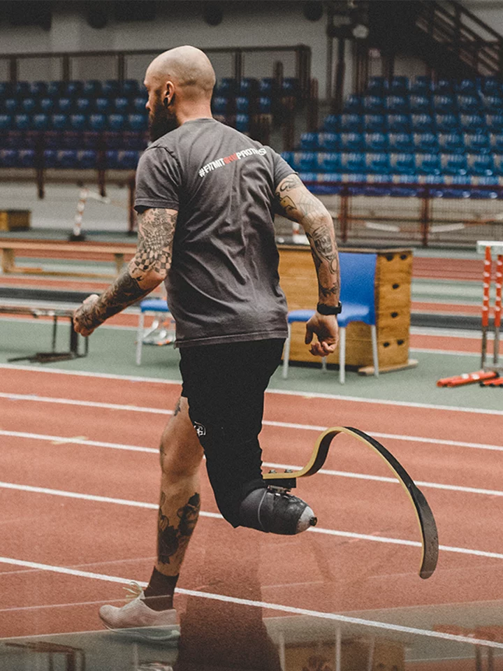 Mitarbeiter und Kunde von APT Prothesen joggt mit einer Sportprothese über Tartanbahn