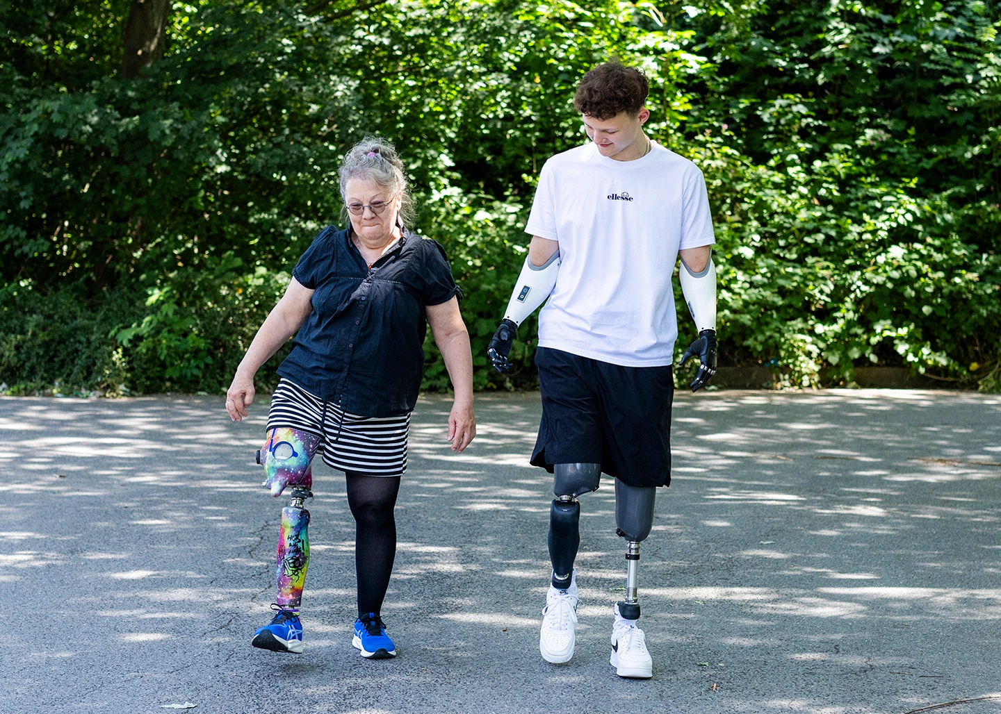 Ein Mann mit zwei Beinprothesen und zwei Armprothesen und eine Frau mit Beinprothese laufen nebeneinander auf einer Straße