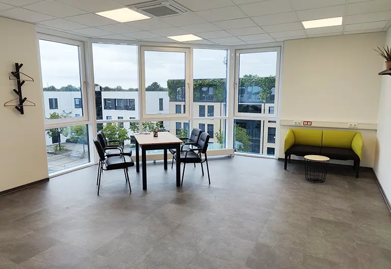 Kundenraum von APT Prothesen in Moers mit Besprechungstisch und grünem Sofa vor heller Fensterfront.