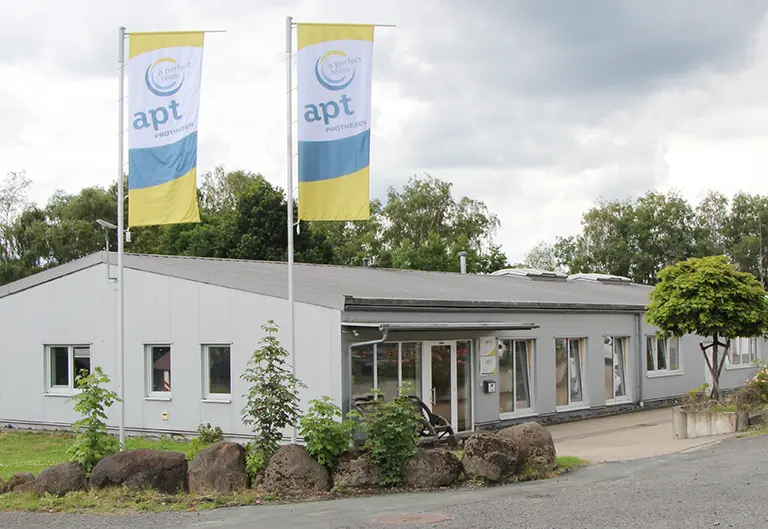 Außenansicht des Gebäudes von APT Prothesen Westerwald. Blick auf den Eingang von der Straße mit Einfahrt.