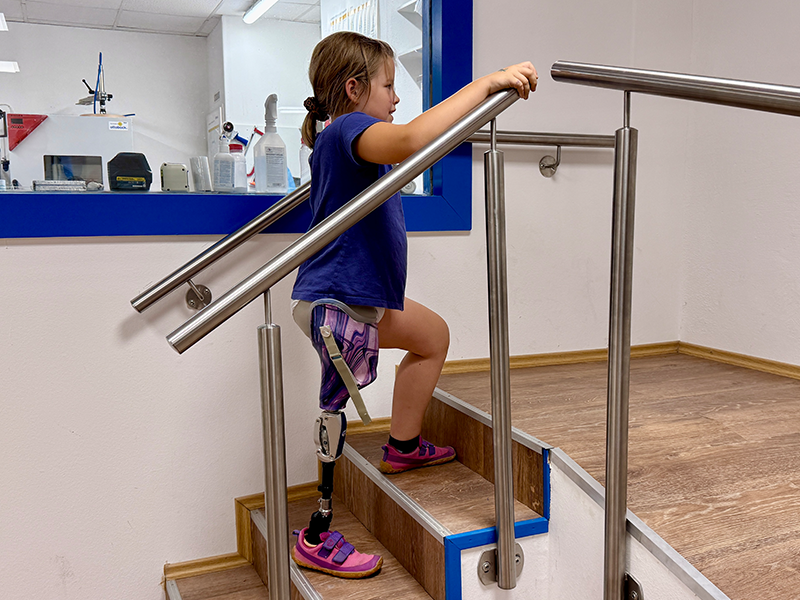 Mädchen mit Beinprothese geht im Anproberaum eine Treppe hoch