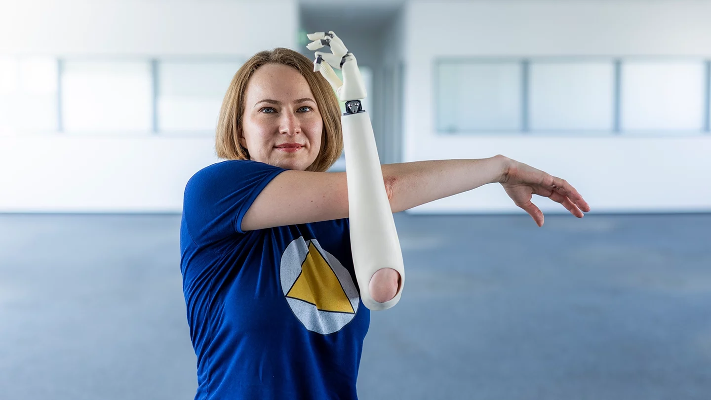 Frau mit Armprothese macht Dehnübung und schaut in die Kamera