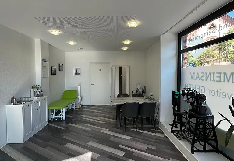 Räumlichkeiten von APT Osthessen in Schlüchtern bei Fulda. Tisch mit Stühlen für Besprechungen mit den Kunden. Medizinische Liege in Grün und High-Board mit Snacks und Getränken für die Kunden.