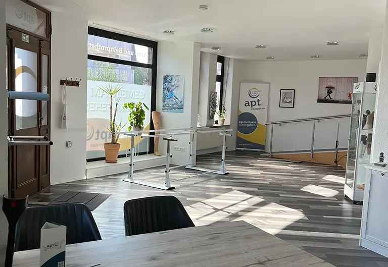 Eingangsbereich mit Geräten von APT Osthessen in Schlüchtern bei Fulda. Es ist ein Barren, Rampe und Vitrine mit Prothesen zu sehen. Helle Fensterfront.