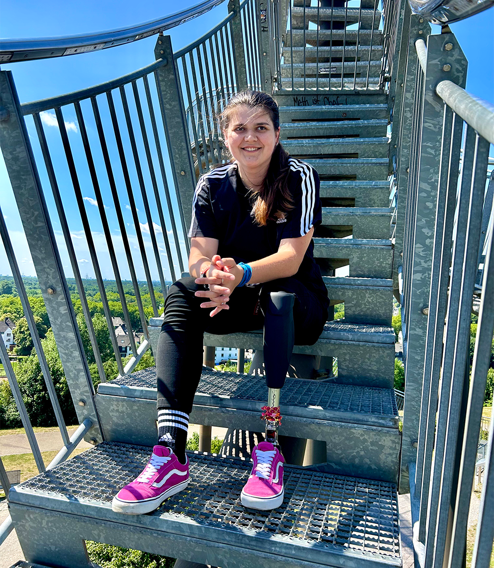 APT Prothesen Kundin Lisa Seidel sitzt in Sportklamotten und mit ihrer Beinprothese auf einer Treppe