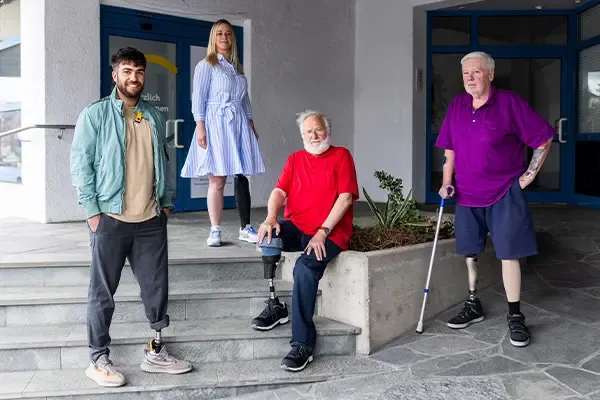 Kunden von APT Prothesen mit Beinprothesen symbolisch stehend vor einer von APTs Standorten für die Reha, Interimsphase und Anpassung der Prothesen.