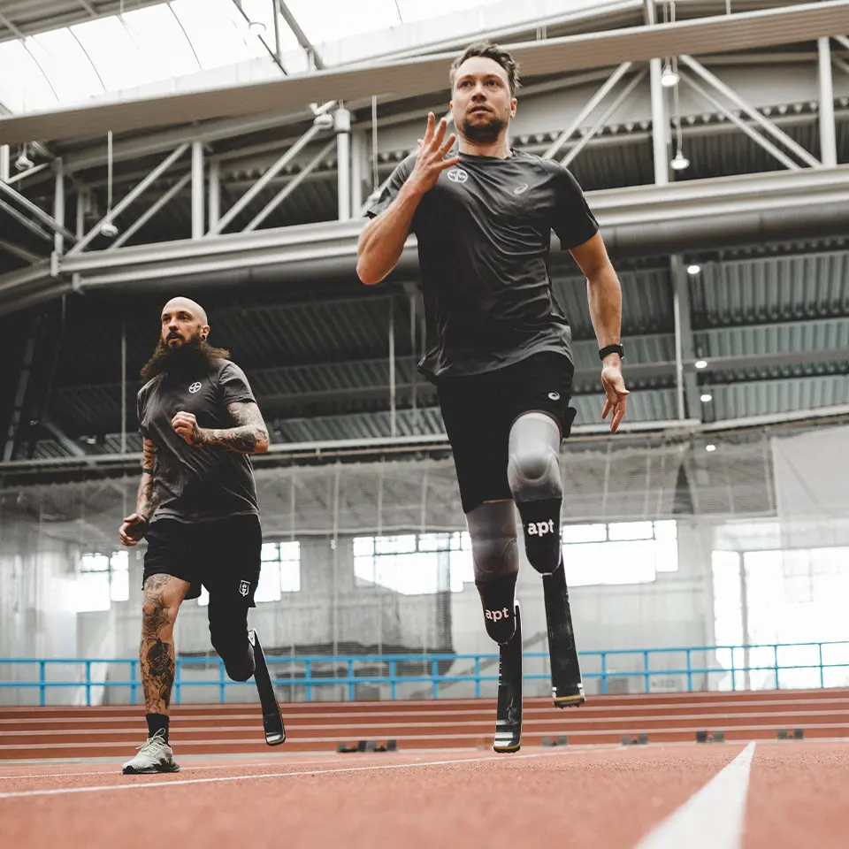 Zwei Männer in Sportklamotten beim Laufen, einer trägt eine Beinprothese zum Laufen, der andere trägt an beiden Beinen Laufprothesen von APT